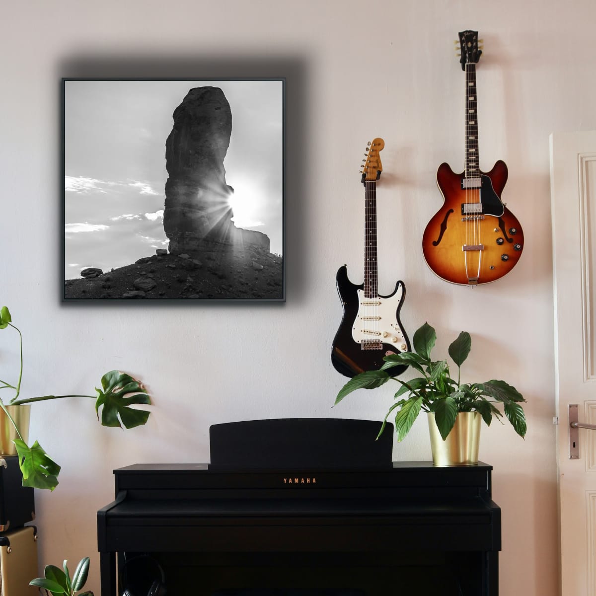 Two guitars on a wall above a piano with a framed picture of a sunlit rock formation.