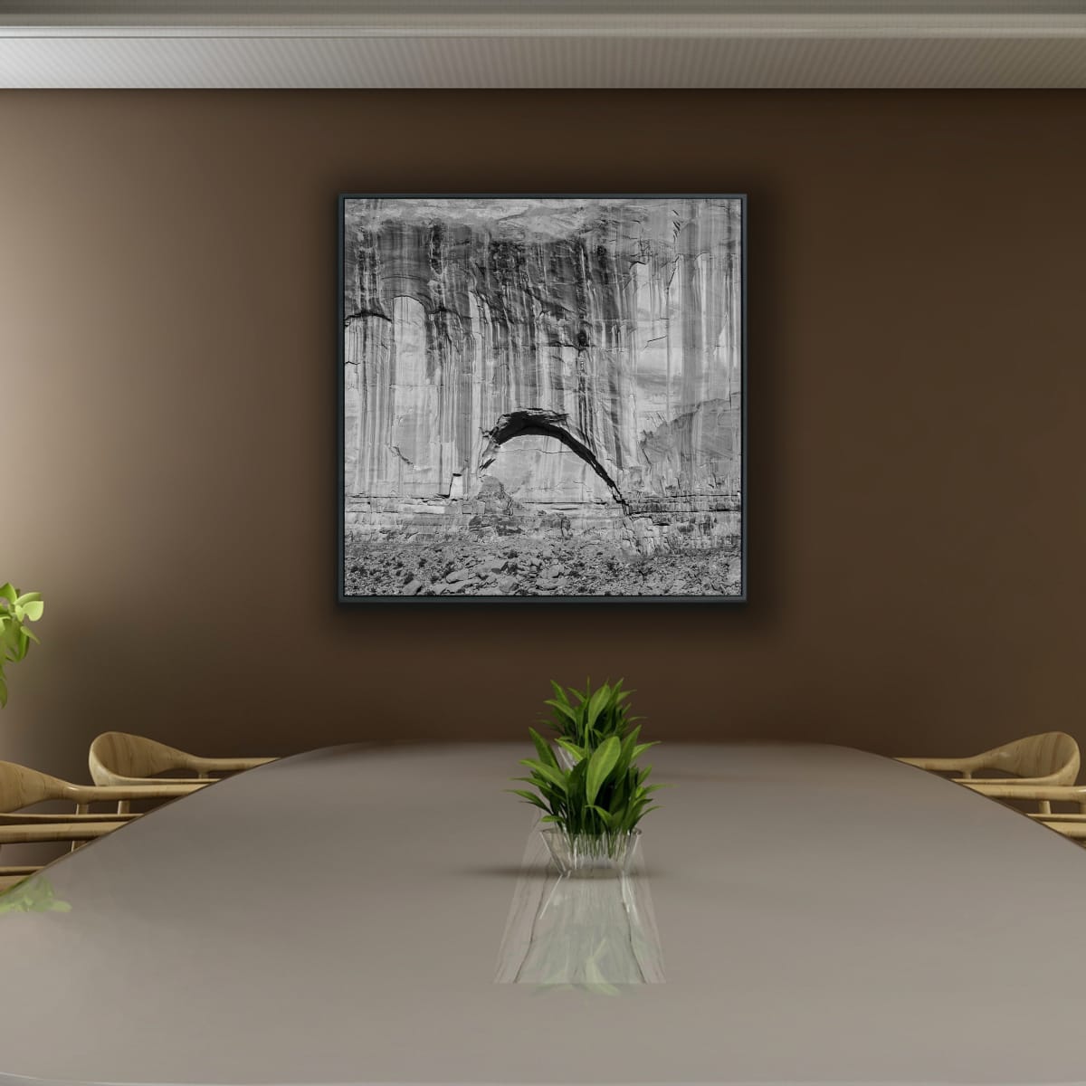 Square black and white 48x48 Monument Valley print of a rock face with an arc formation on a brown wall above a board table with a plant.