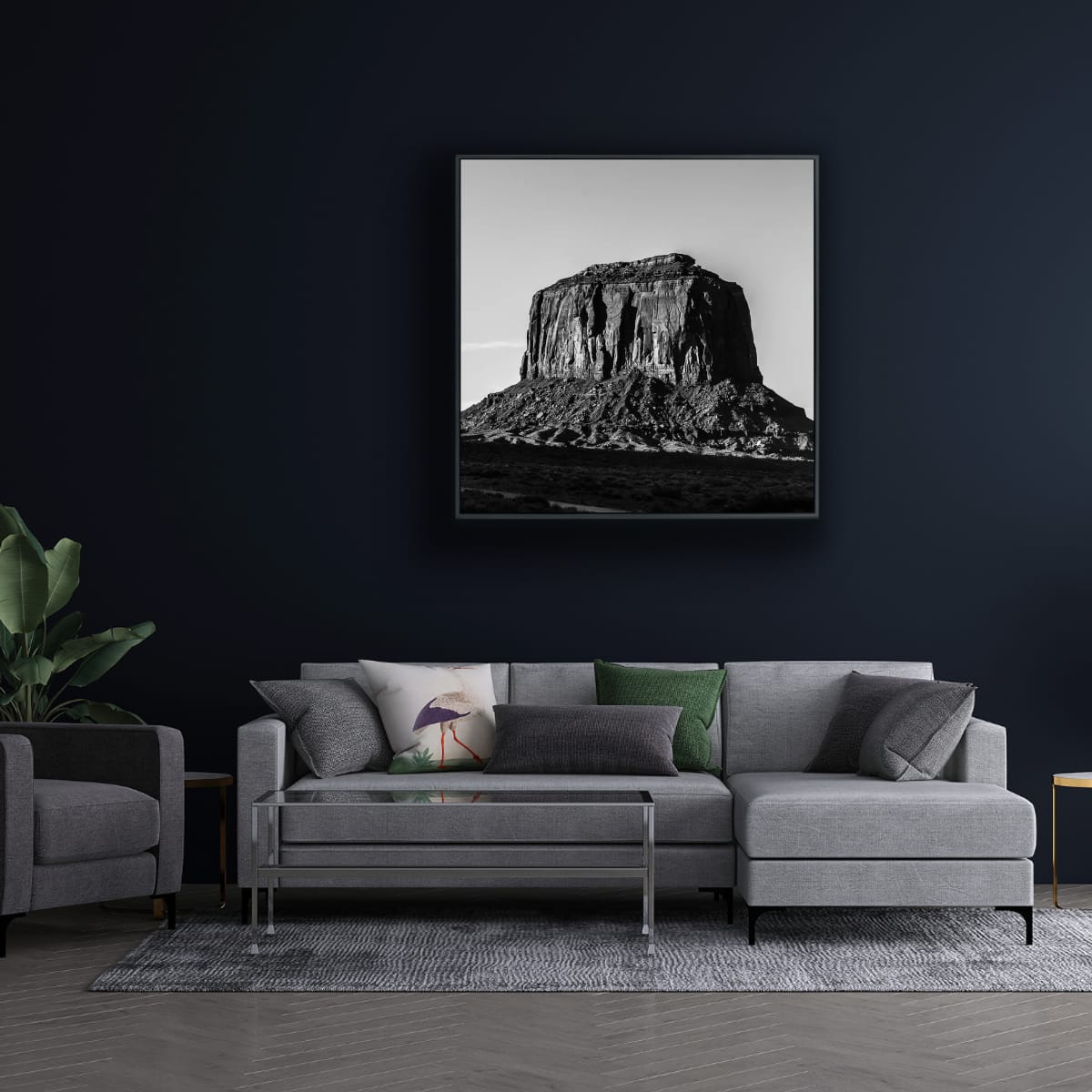 Living room with a gray sectional sofa, armchair, and framed black and white photograph of a large rock formation against a clear sky hanging on darkly painted wall.