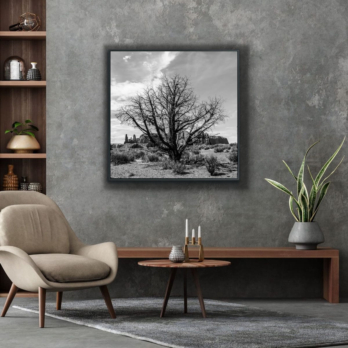 Living room with a framed black and white photograph of a lone dried tree in foreground, Monument Valley in distance, on a gray wall, a beige armchair, a wooden side table, and a plant.
