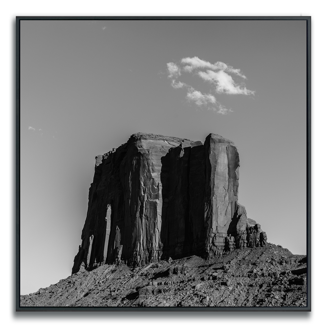 Framed black and white square metal print of a Monument Valley solitary butte with a single sparse cloud formation in the sky above it.