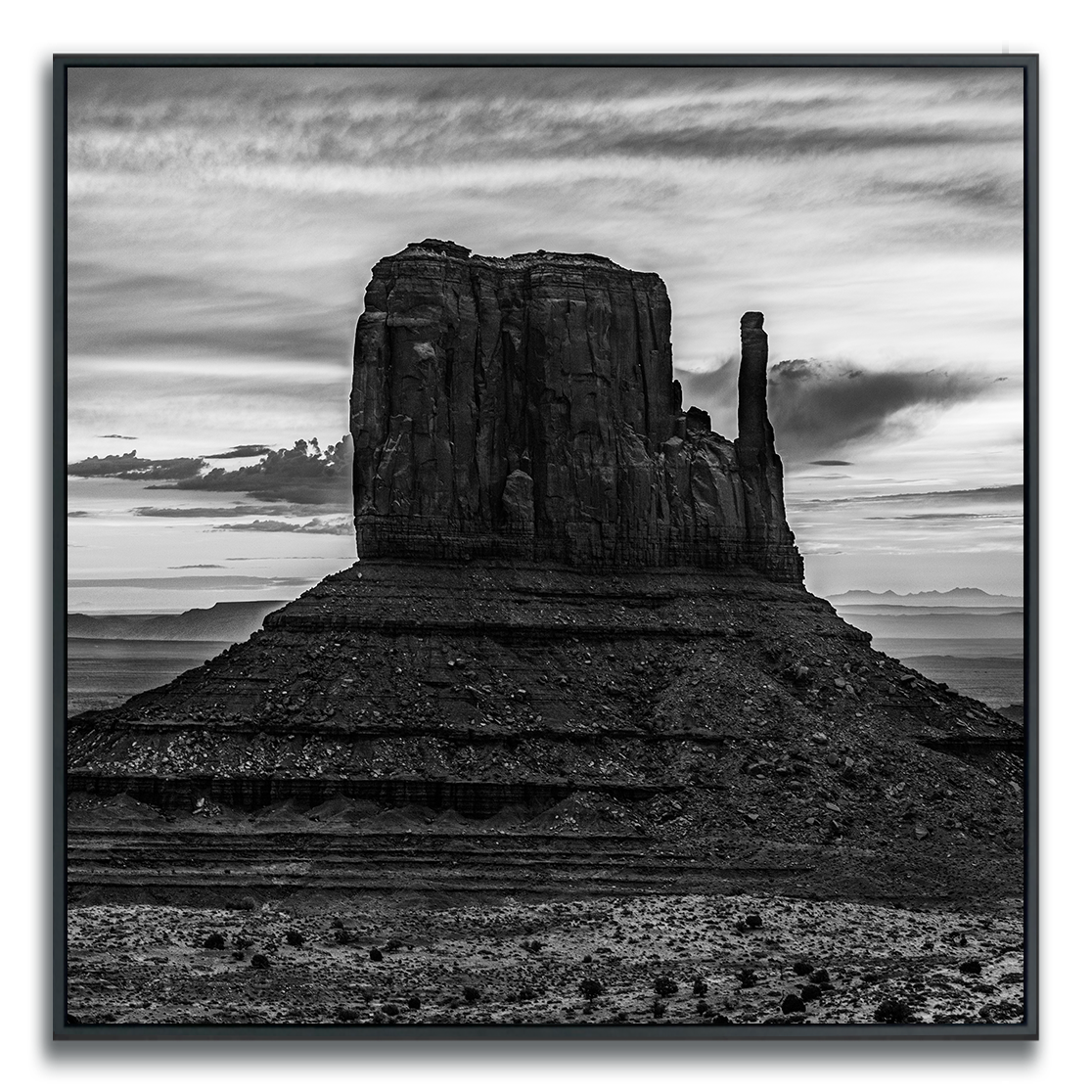 Black and white photograph of Monument Valley iconic desert butte shadowed against dramatic desert sky.