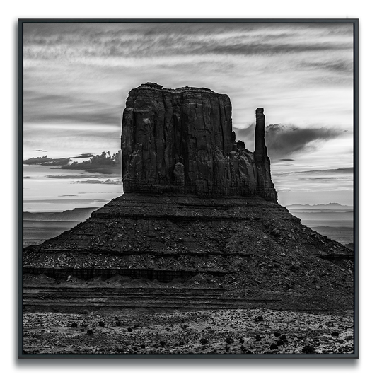 Black and white photograph of Monument Valley iconic desert butte shadowed against dramatic desert sky.