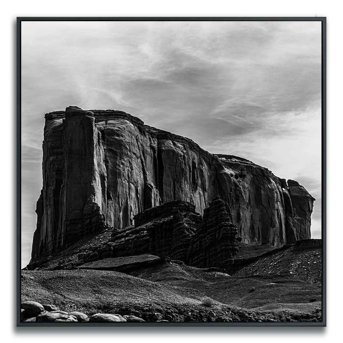 Black and white photograph of Monument Valley Rock Ridge framed dramatically under a wispily cloud covered sky.