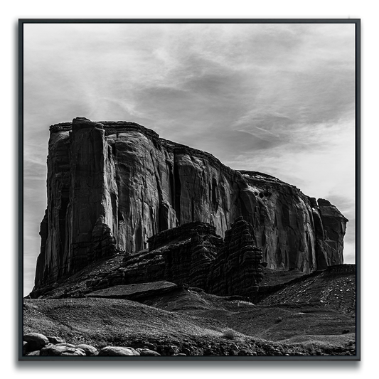 Black and white photograph of Monument Valley Rock Ridge framed dramatically under a wispily cloud covered sky.