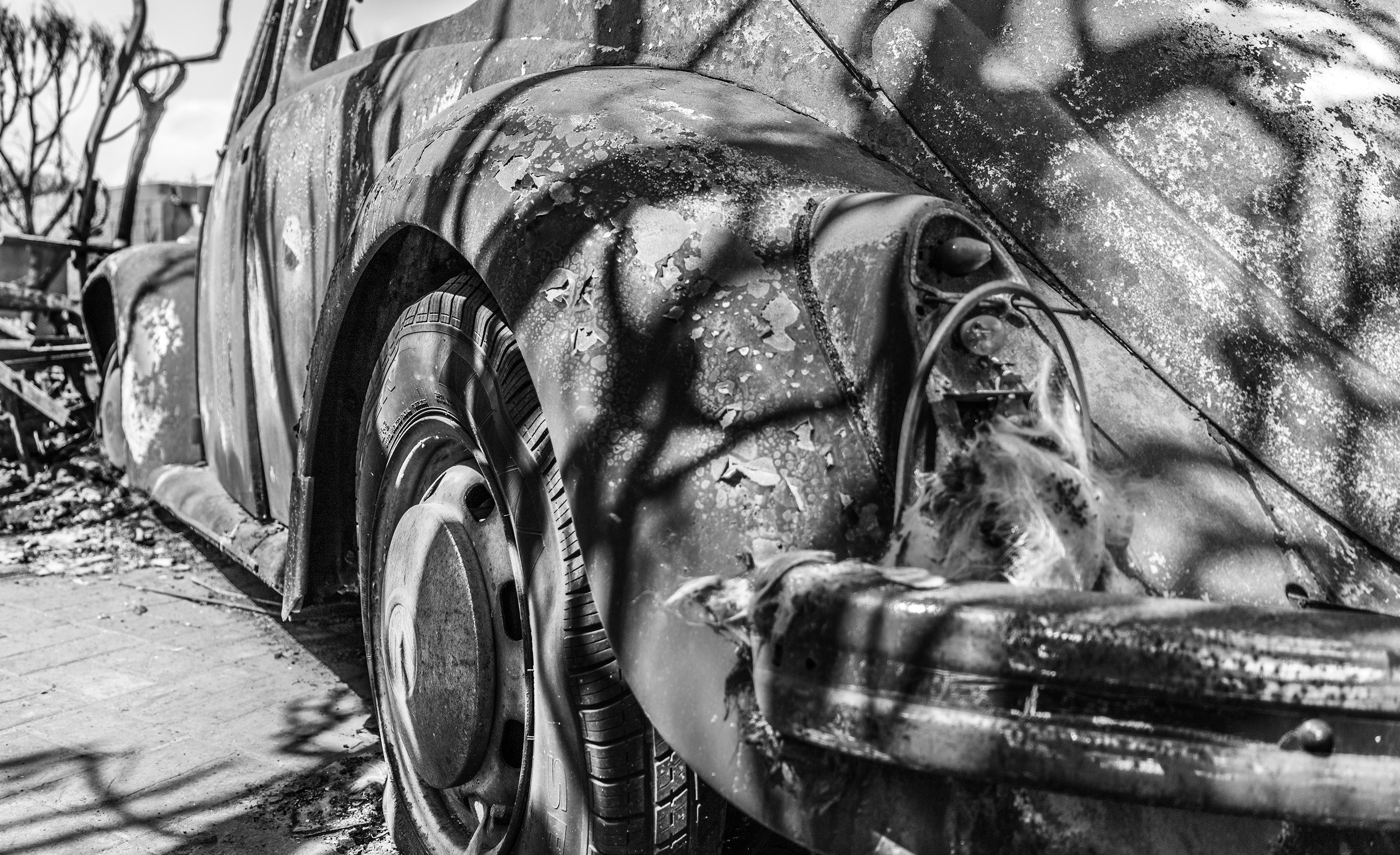 Black and white fine art photograph burnt car with dark tree shadows over it