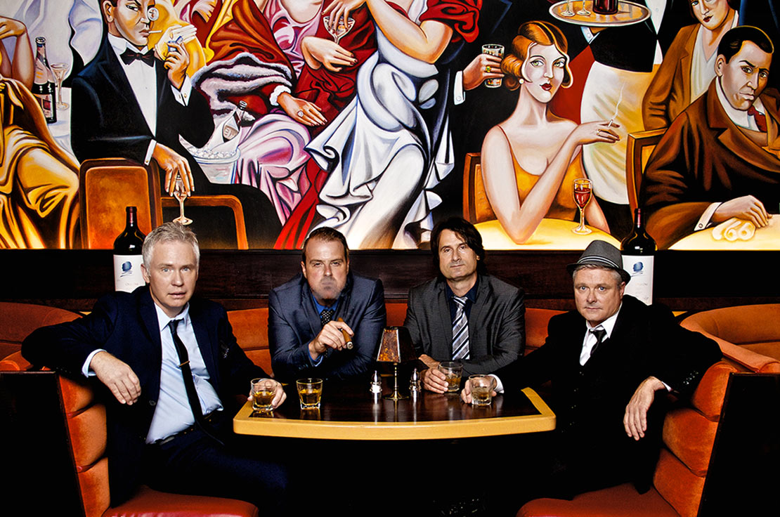 Band photo Nashville The Eventuals four members sitting in restaurant booth art deco mural painted on wall behind them