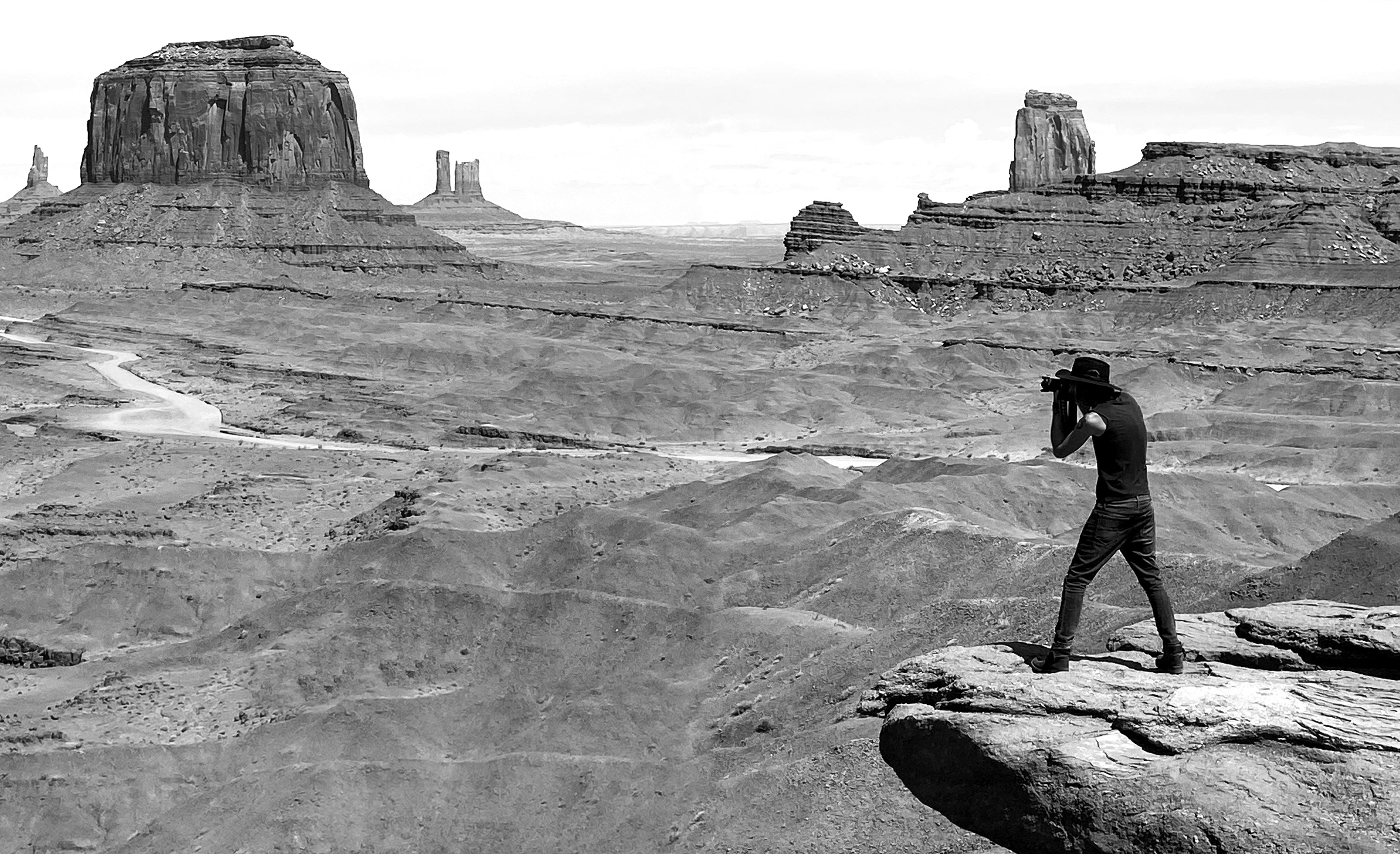 black and white photo photographer Mark Maryanovich taking a photo while standing on cliff edge in Monument Valley 