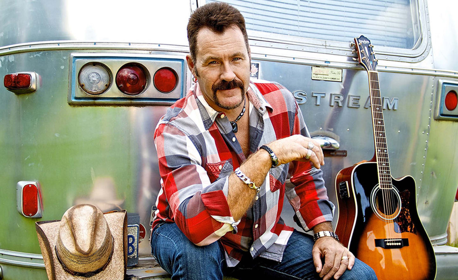 Country Music Artist photo Dean Young sitting on back of airstream trailer acoustic guitar and cowboy hat on bumper beside him