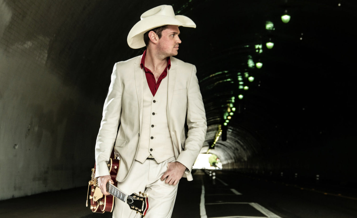 Country Music Portrait Los Angeles Ben Klick standing in tunnel wearing white suit red shirt white cowboy hat green lights on roof of tunnel beside him