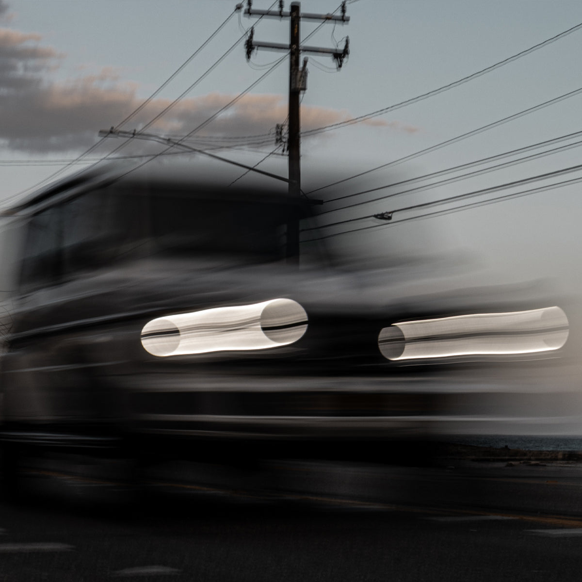 Blurred image of a vehicle's front lights with power lines in the background