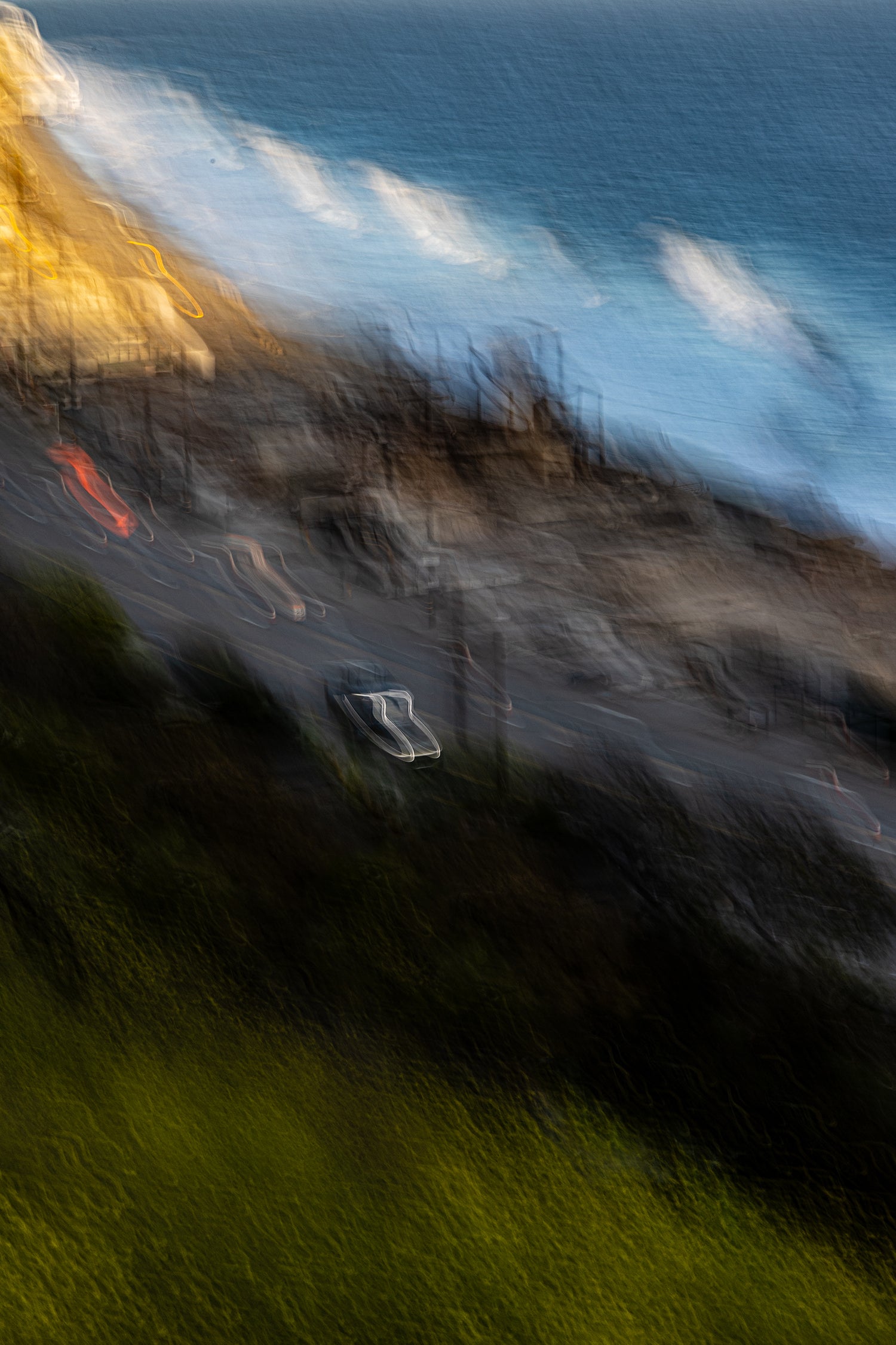 Abstract long‑exposure photograph of a coastal highway at night, with blurred lights suggesting waves and motion along the shoreline.