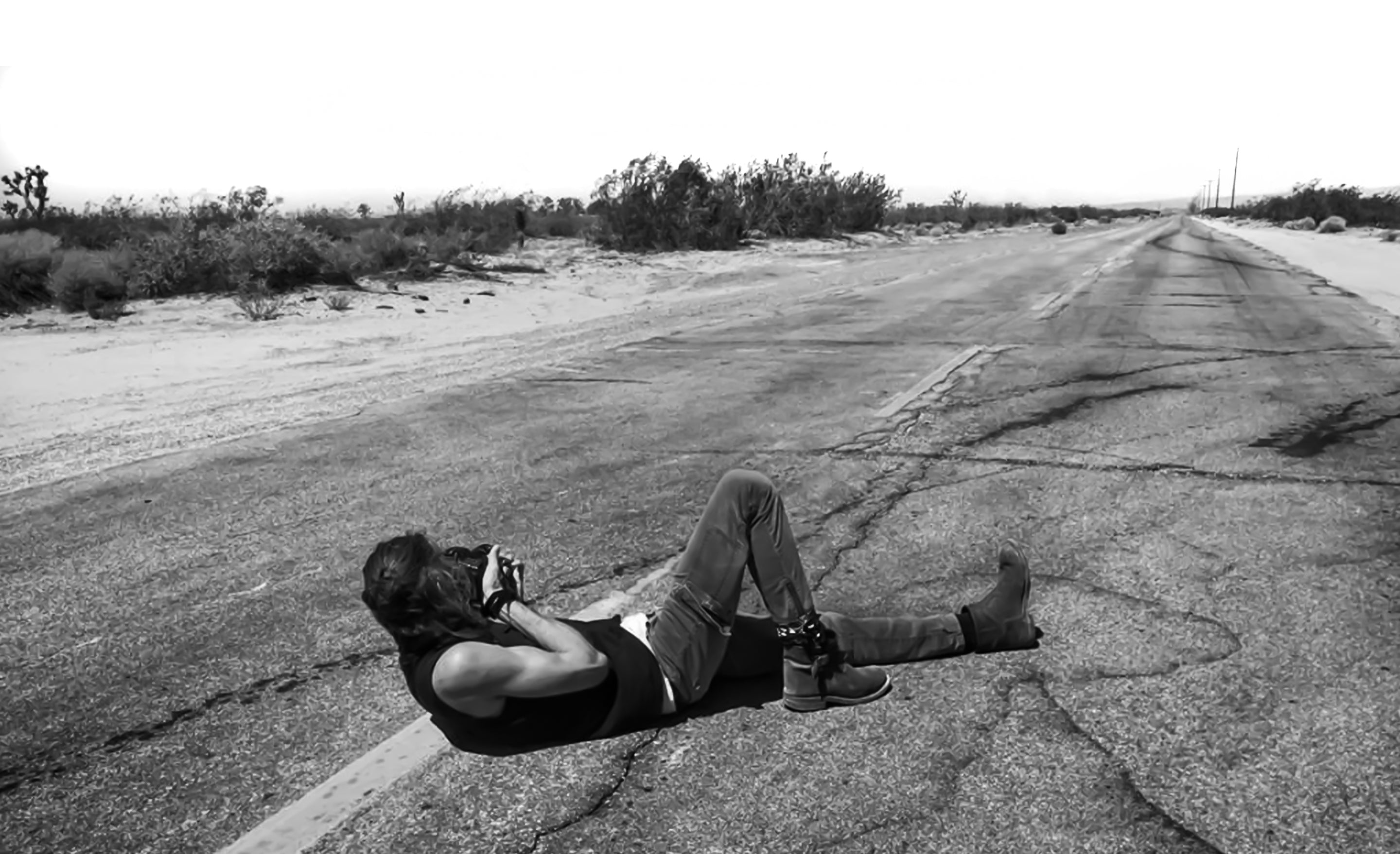 Fine art portrait photographer Los Angeles based March Maryanovich lying in middle of road looking through back of camera at road ahead in black and white