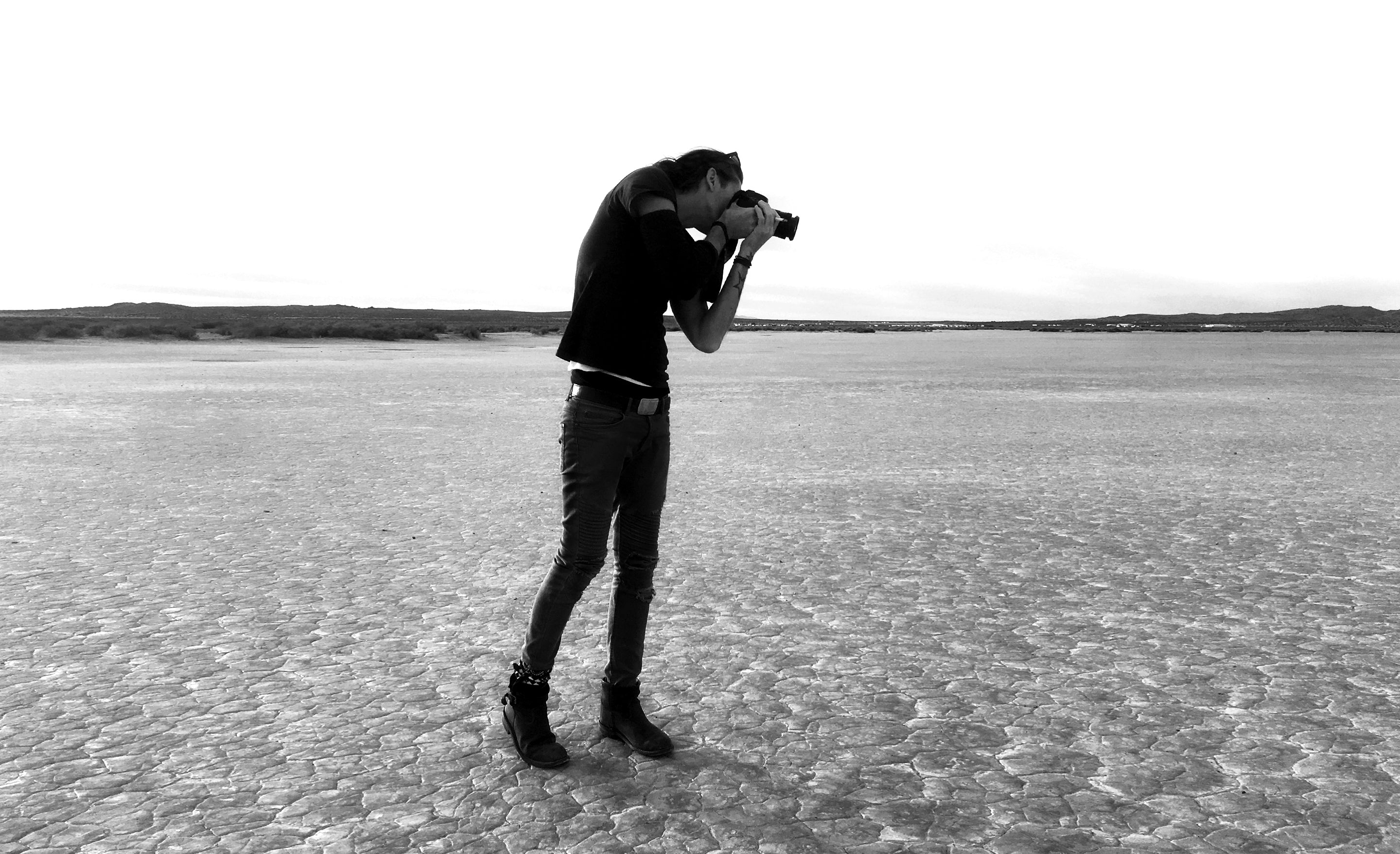 Los Angeles Fine Art Photographer Mark Maryanovich promotional Image standing on dried lakebed holding camera black and white