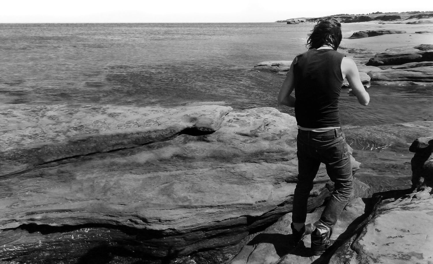 Mark Maryanovich standing on a rocky shoreline with water in the background 