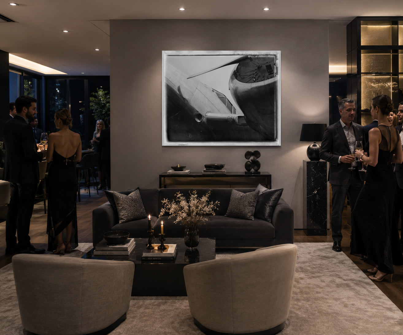 A large black and white framed art print depicting a sleek car, displayed on a gray wall in a modern, dimly lit social lounge with guests mingling around a dark sofa and armchairs.
