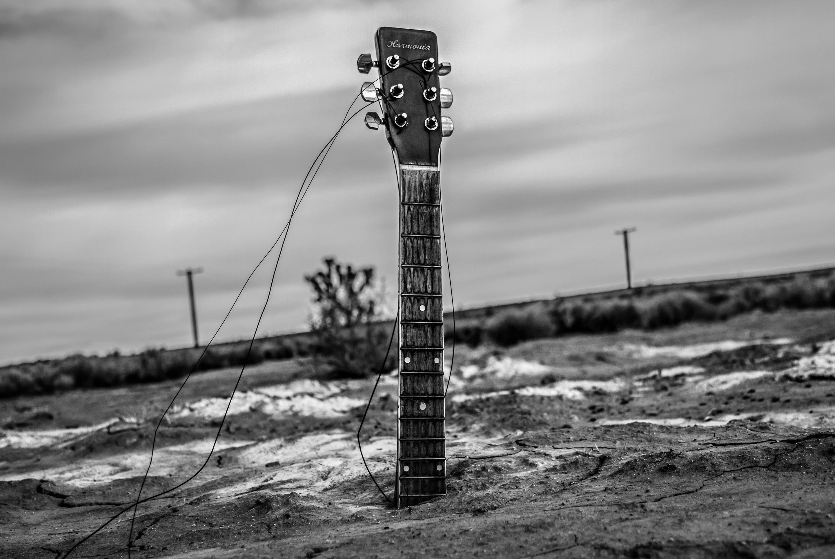 Fine art black and white photograph guitar neck protruding from body buried in desert sand