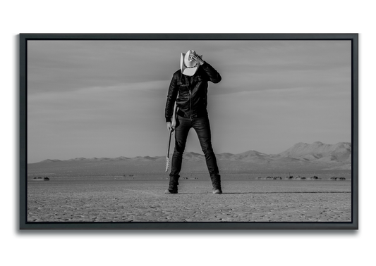 Black and white fine art photographic metal print man standing in desert holding guitar head down with hand keeping his white cowboy hat in place