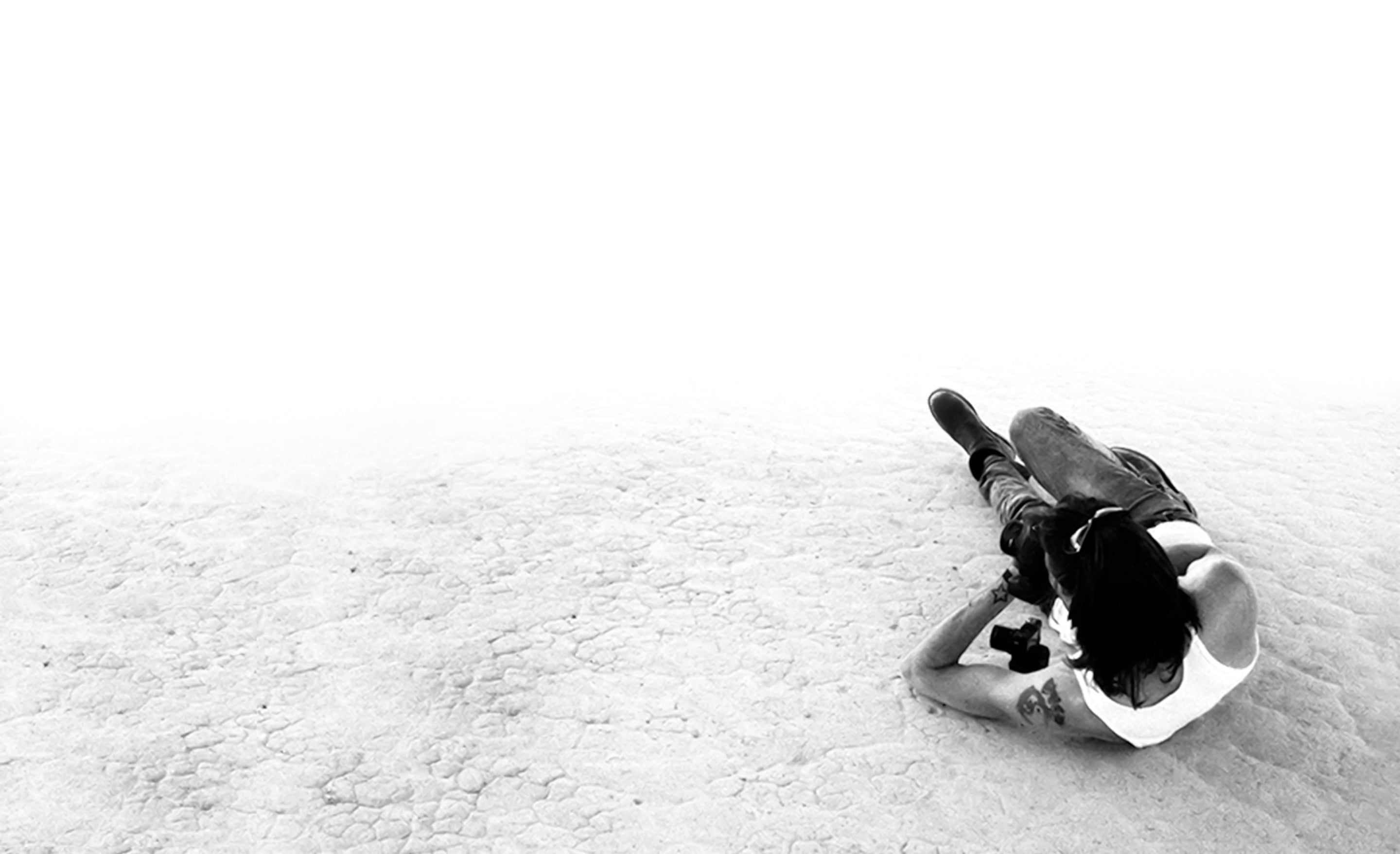 Los Angeles Fine Art Photographer Mark Maryanovich promotional Image lying on dried lakebed holding camera black and white from overhead perspective