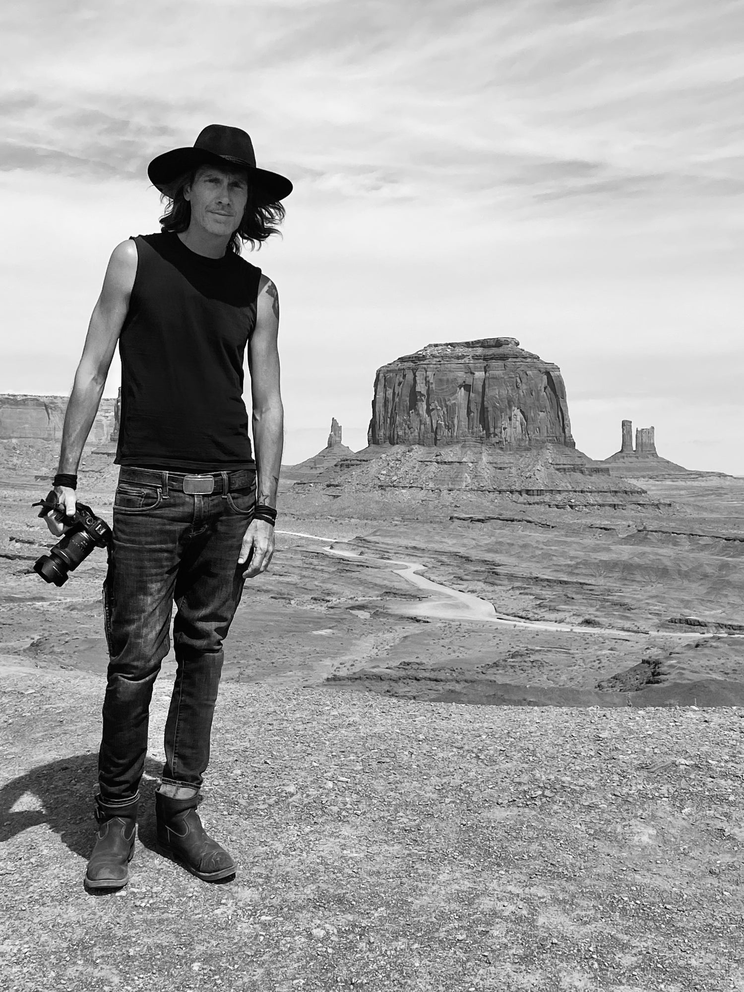 Black and white photo Mark Maryanovich standing in Monument Valley holding camera