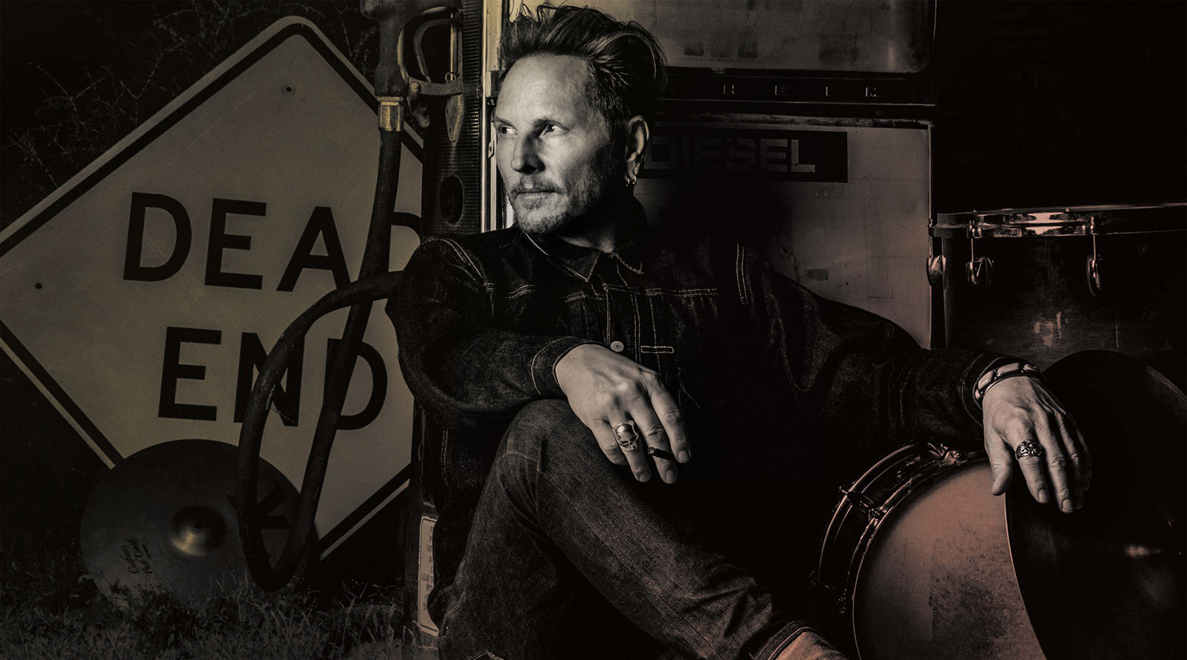 Matt Sorum portrait sitting against gas pump drum kit beside him