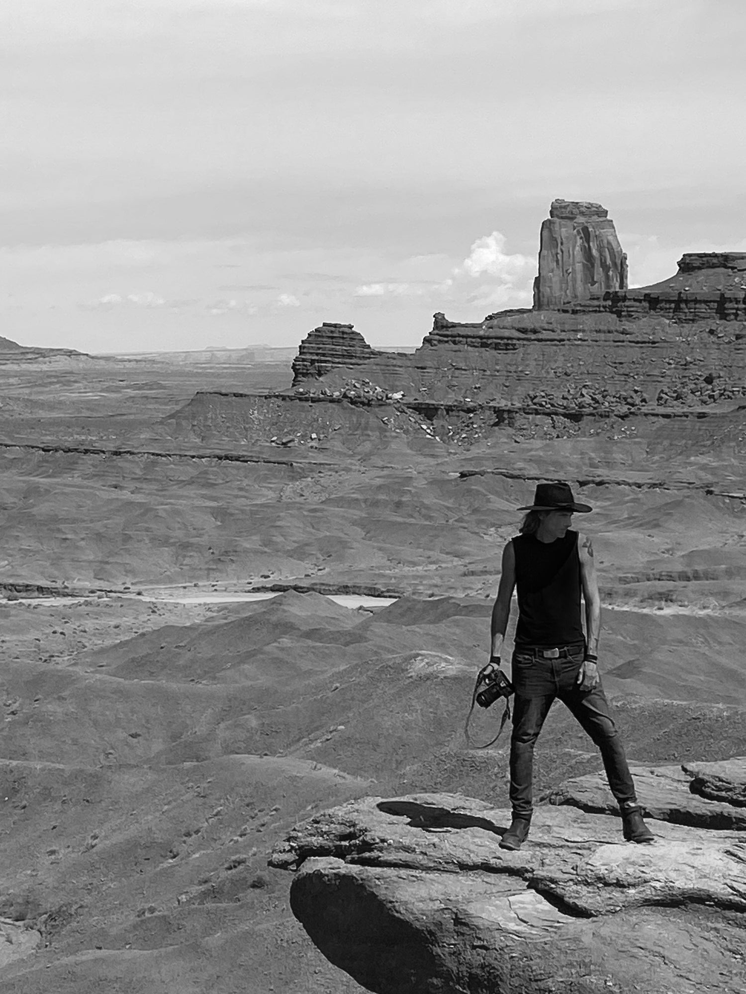 Black and white photo Mark Maryanovich standing at cliff edge in Monument Valley holding camera