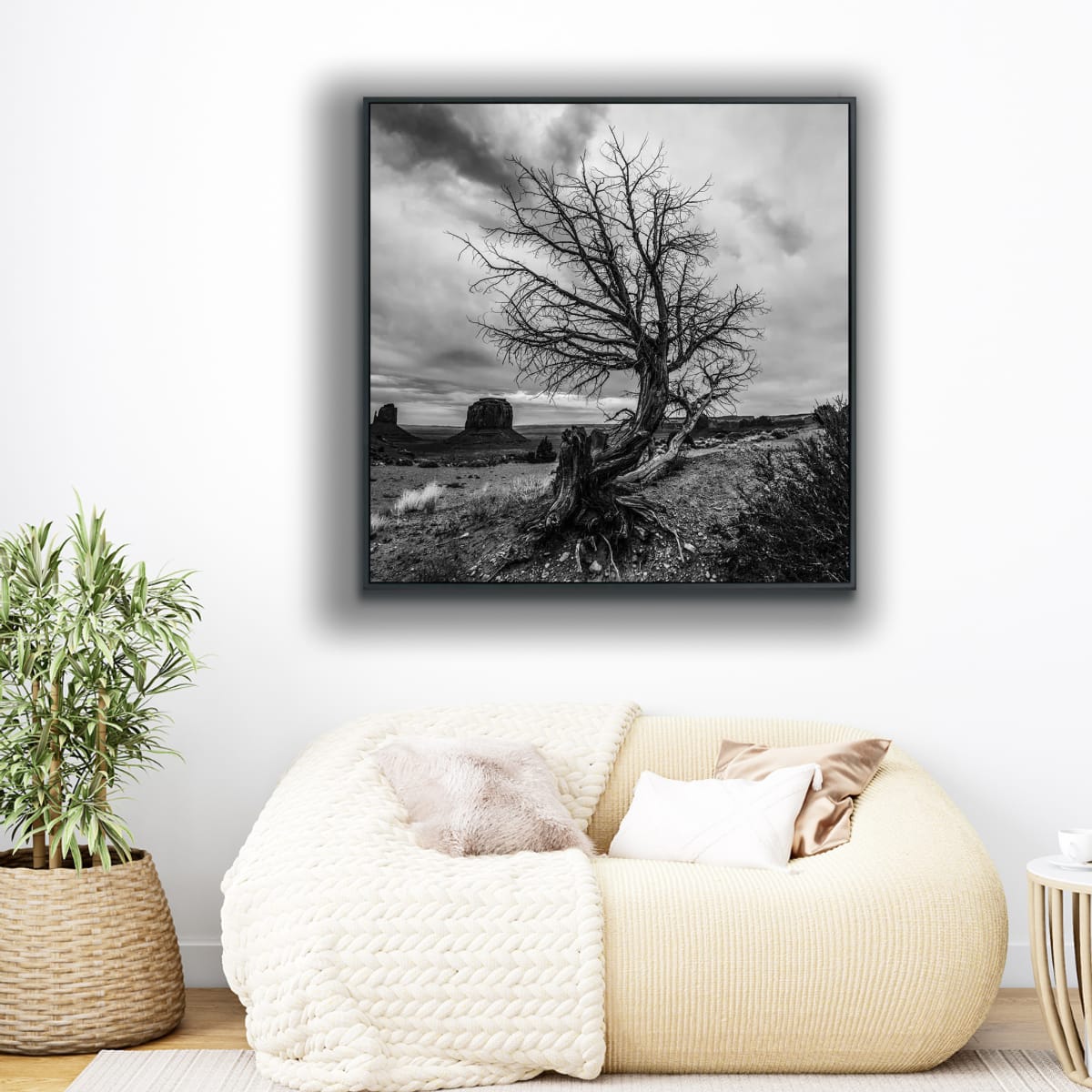 Framed black and white landscape print above a rounded love seat featuring a black and white photograph of a lone curved tree in foreground, iconic Monument Valley buttes in background.