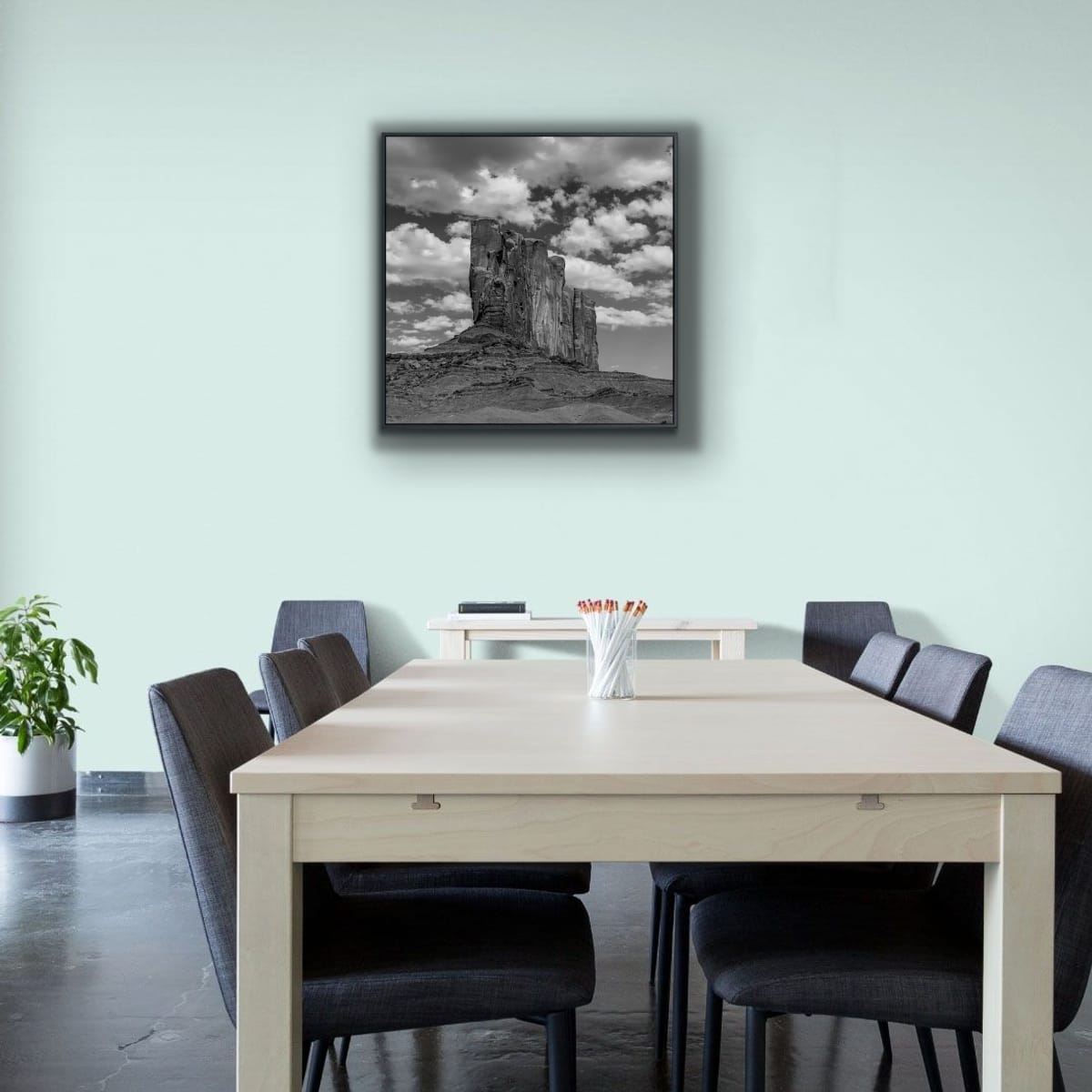 Boardroom with a light wood table and black chairs, featuring a framed black and white square print of a Monument Valley Butte on the wall.