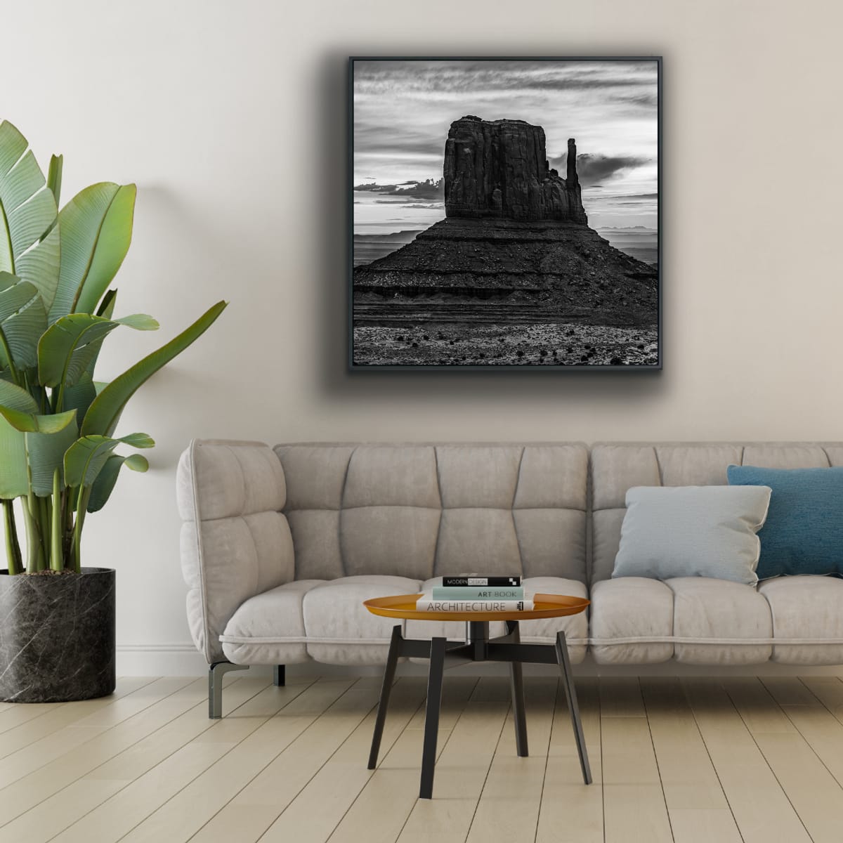Living room with a beige sofa, small round table, and a framed black and white photograph of Monument Valley iconic desert butte shadowed against dramatic desert sky.