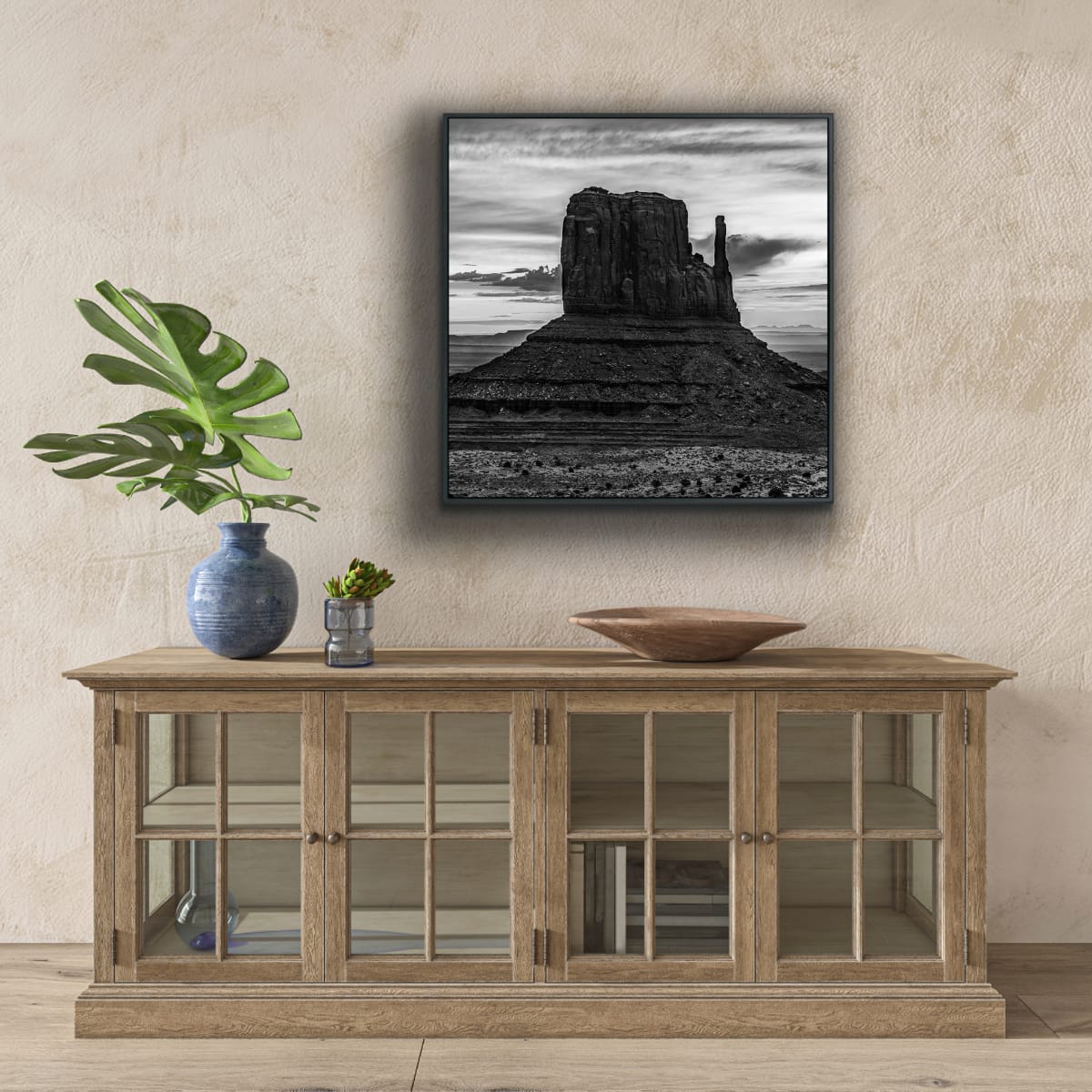 Wooden credenza with glass doors, decorative items, and a framed black and white photograph of Monument Valley iconic desert butte shadowed against dramatic desert sky.