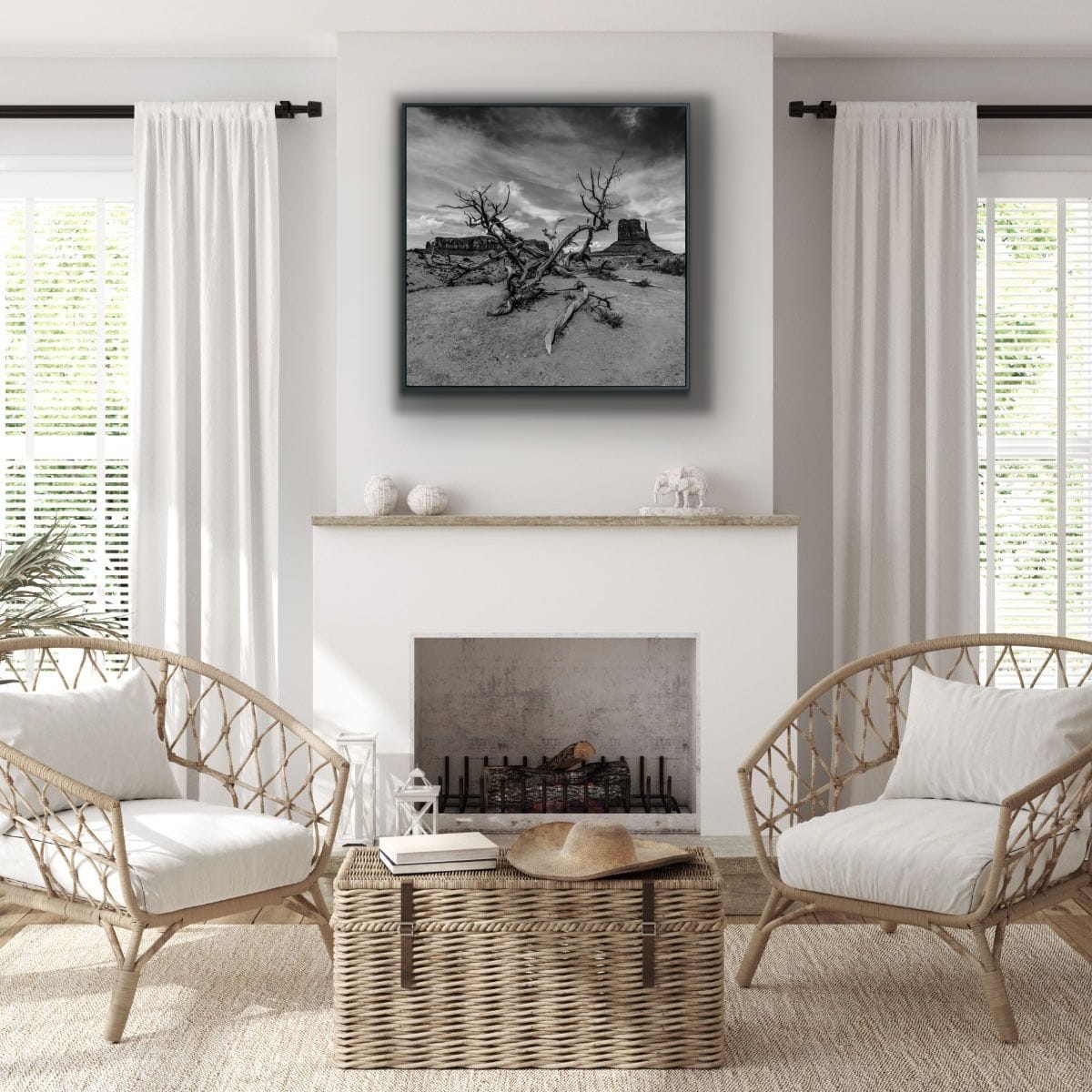 Living room with wicker chairs, a coffee table, and fireplace below the 48x48 black and white metal print of a desert with a dead tree and Monument Valley in the background.