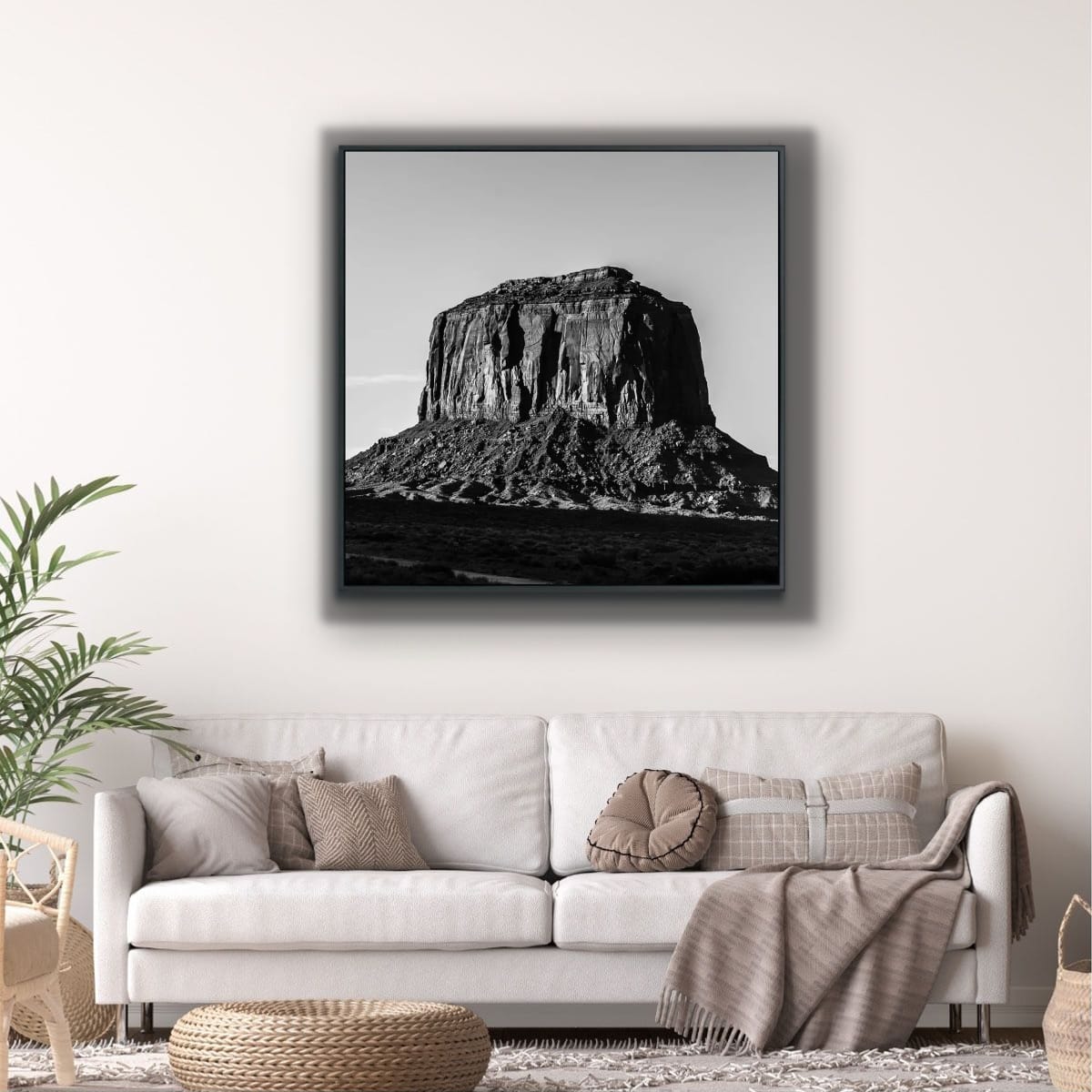 Framed black and white photograph of a large rock formation against a clear sky above a white sofa in a living room with beige walls.