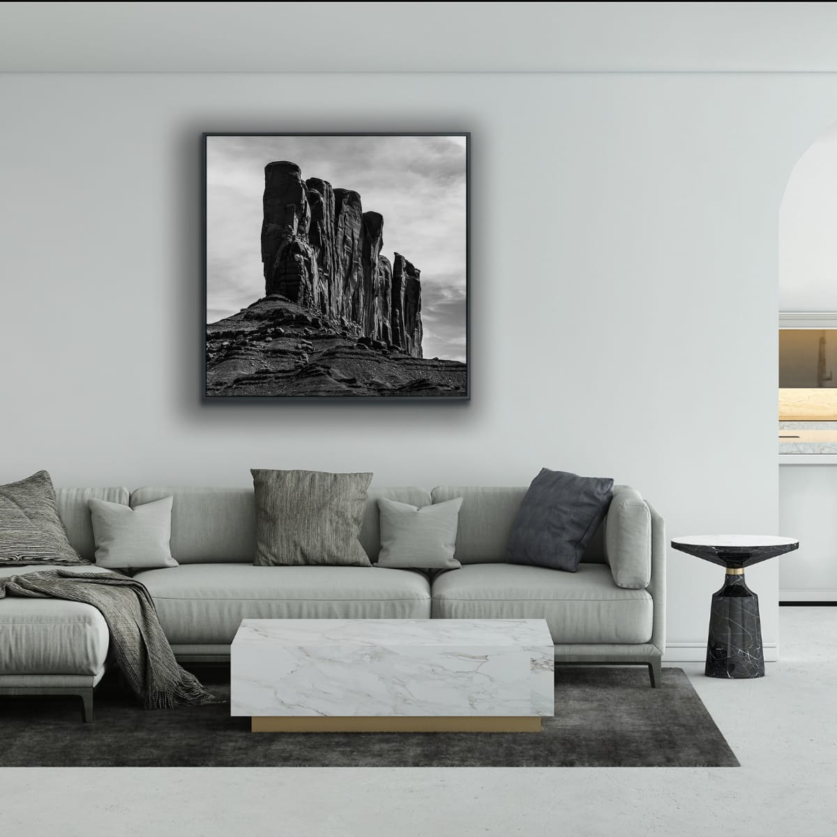 Living room with a gray sofa, marble coffee table, and a large framed black and white photograph of a rocky landscape with tall rock formations against a cloudy sky on white wall.