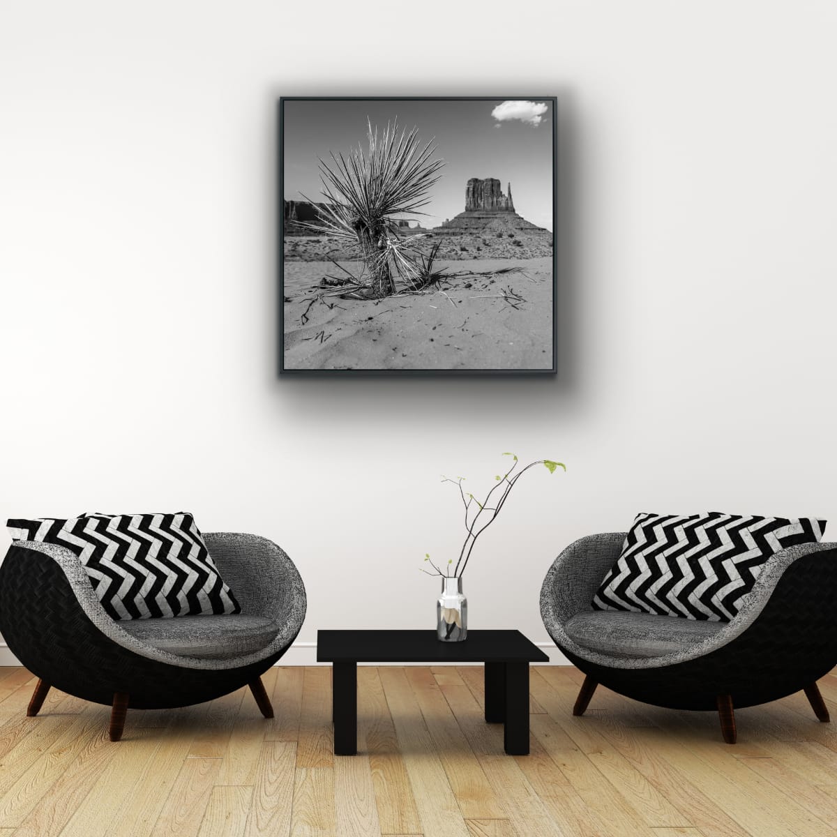Living room with two black and gray chairs with zigzag matching throw pillows, a small table, and a framed black and white landscape print on the wall featuring  a black and white photograph of a desert landscape with a cactus and iconic Monument Valley butte in the background.