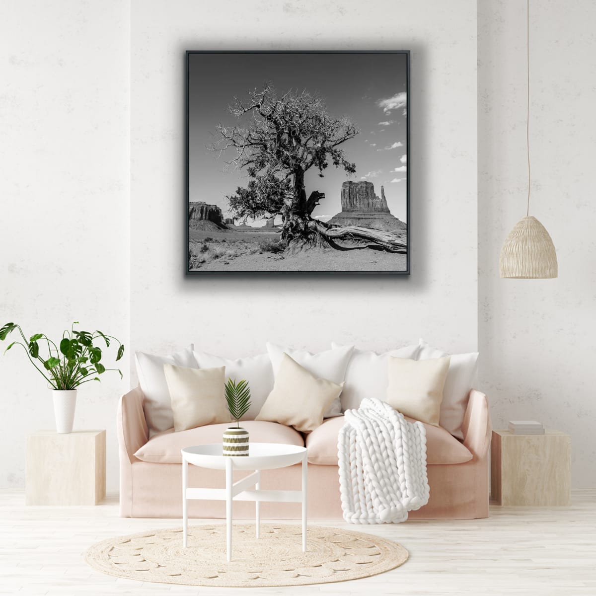Framed fine art black and white photograph of a dried desert tree, iconic Monument Valley buttes in background above a soft pink sofa in a minimalistic livingroom.