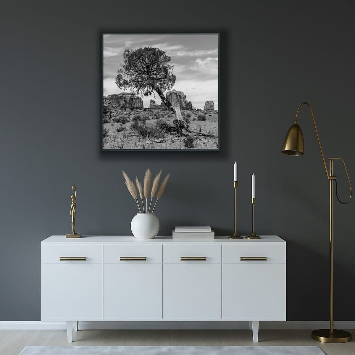 Modern interior with a white cabinet, decorative items, and a framed black and white print on a dark wall, featuring a lone slanted tree Monument Valley rock formations in background.