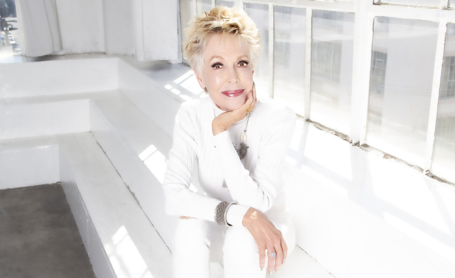 Jan Daley Portrait sitting on white steps wearing all white