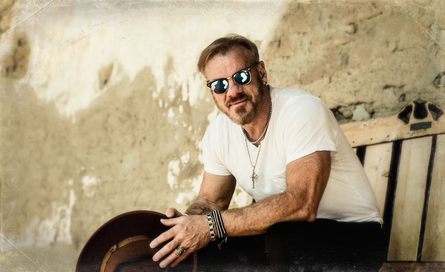 Musician portrait Phil Vassar  wearing white t shirt holding hat sitting on park bench