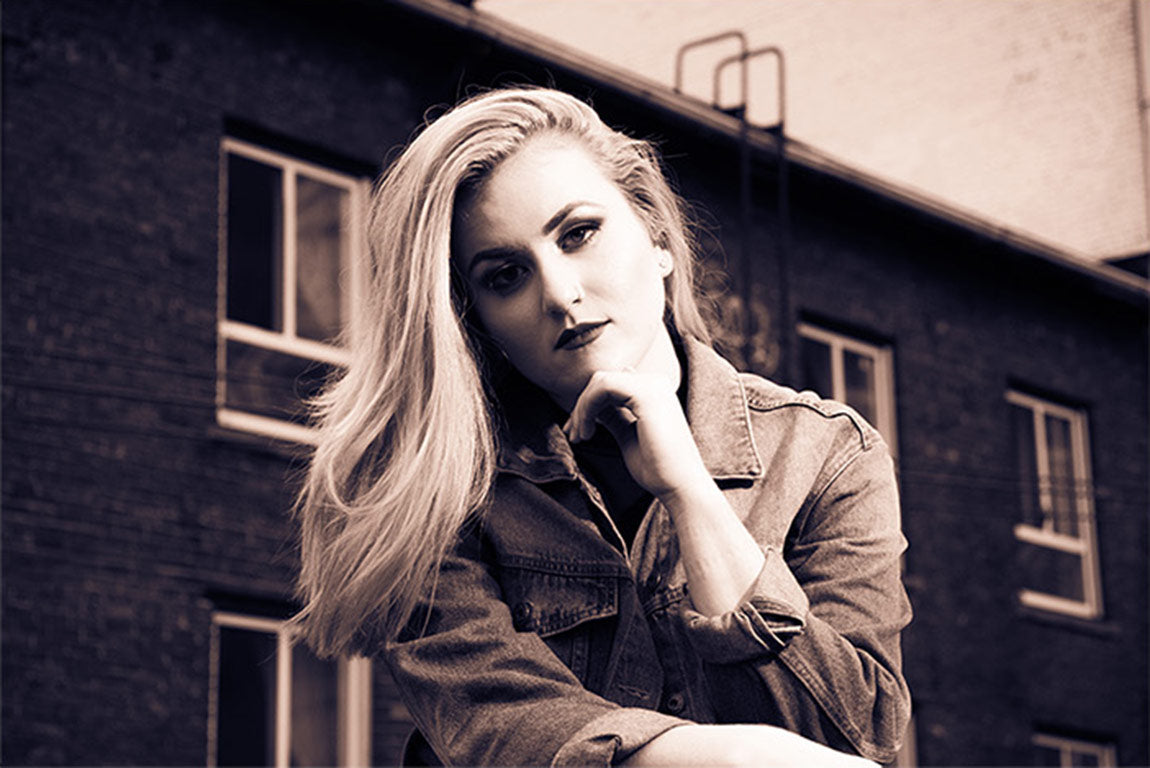 Musician portrait example Artist Development Program Molly Aspinall toned black and white sitting in front of building with chin resting on hand