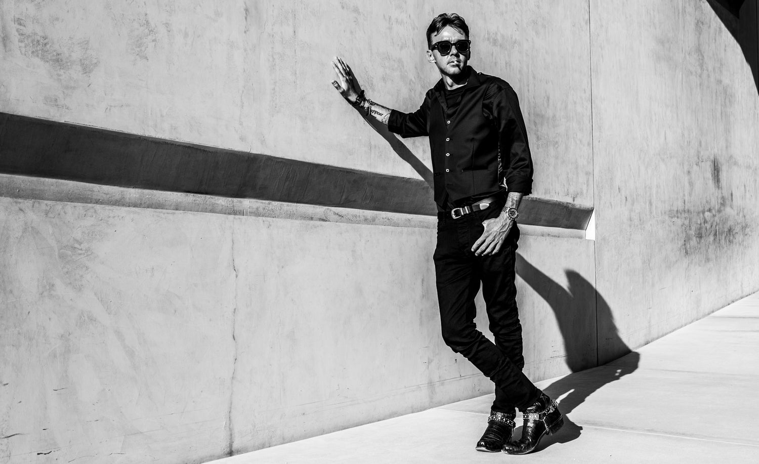 Male musician portrait Chandler Morrison black and white leaning against concrete wall smoking cigarette