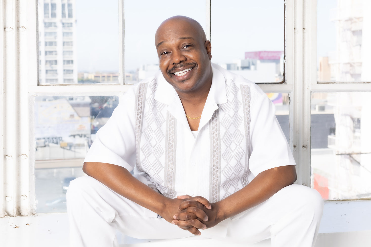 Musician portrait Kenneith Perrin sitting in front windows wearing white