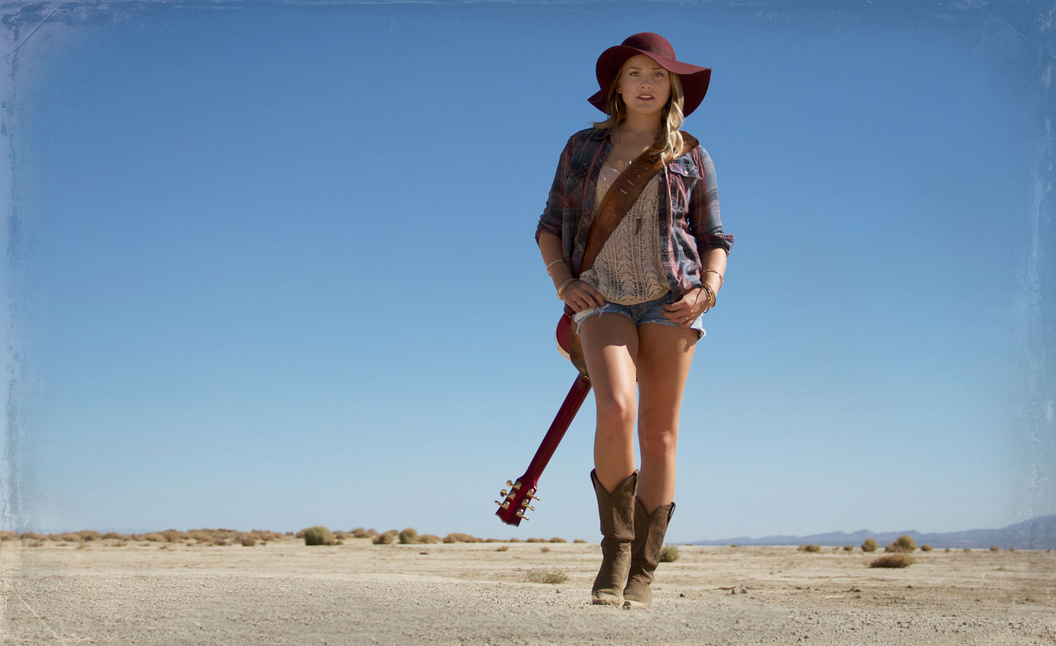 Musician portrait Danielle Marie walking in desert guitar slung across her shoulder