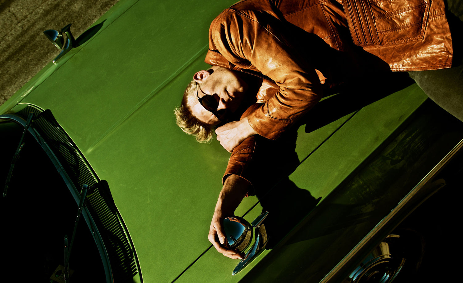 Musician photo Ryan Guldemond lying on hood of green vintage car wearing orange coat and sunglasses Route 66