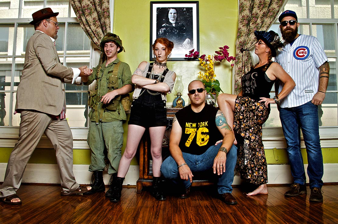 Nashville band photo Amelia Eisenhauer And The Peruvian Farm Girls six band members standing against lime green wall with patterned curtains