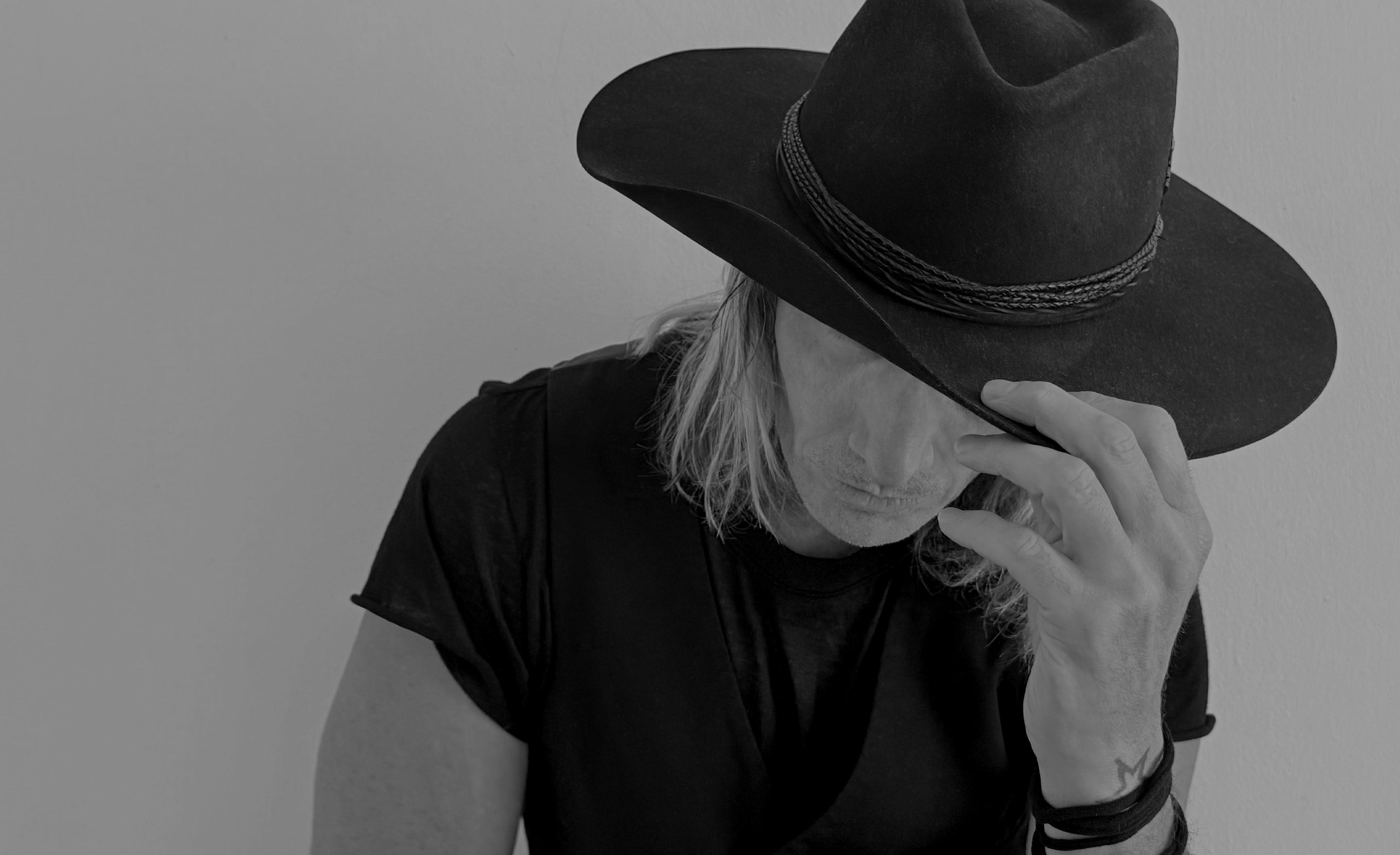 Los Angeles Portrait Photographer Designer Mark Maryanovich wearing black bespoke hat in black and white looking down while touching wide corner curled brim