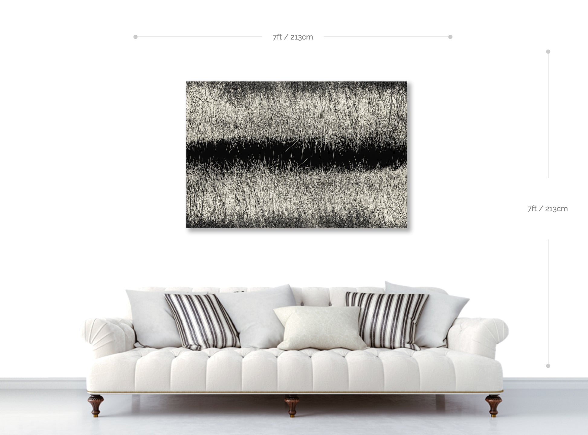 White sofa with striped cushions in front of a black and white landscape painting on a white wall.