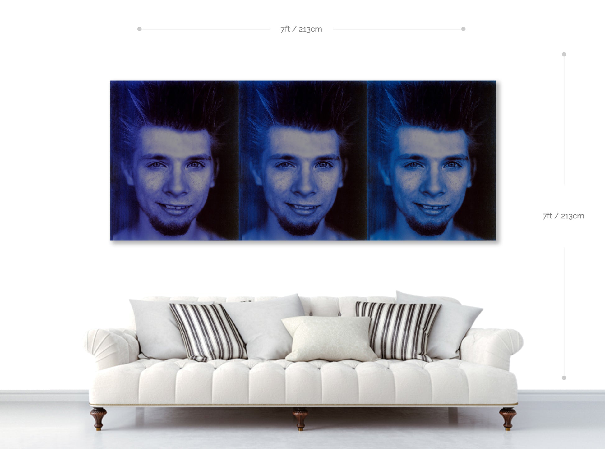 Three-panel wall art of a person's face above a white sofa with striped cushions.
